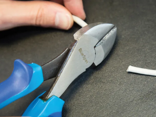 Blue and black pliers being used to cut a white cable on a dark surface