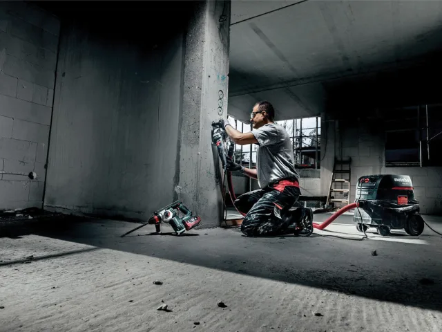Person using a power tool in an industrial setting with concrete walls and floor.