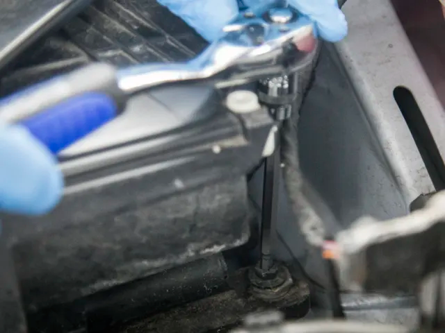 Close-up of a person using a tool on a mechanical component, wearing blue gloves.