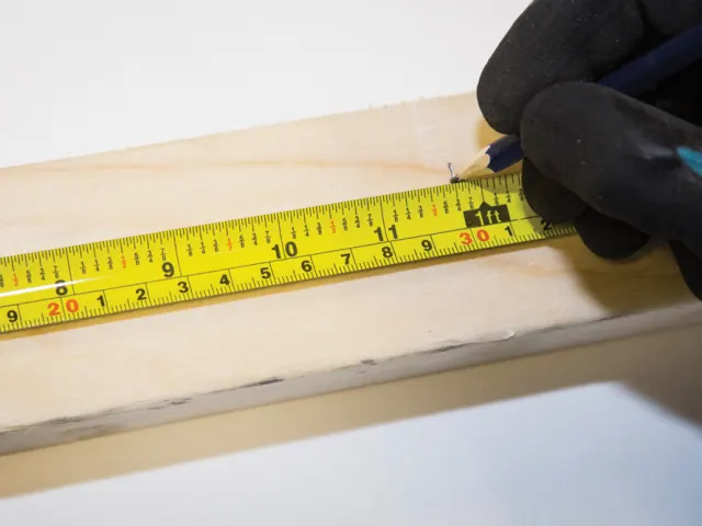 Hand holding a yellow measuring tape on a wooden surface