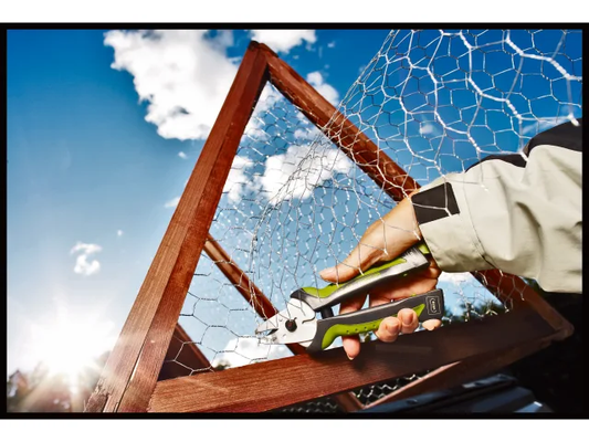 Person using garden shears on a wooden frame with a blue sky background