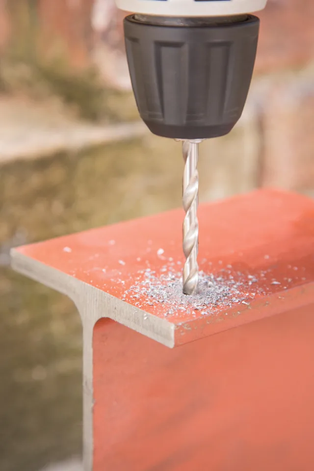 Drill bit drilling into a concrete block with a blurred outdoor background