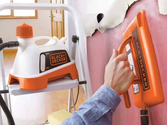 Person holding a Black+Decker handheld sprayer with a step stool and cleaning supplies in the background.