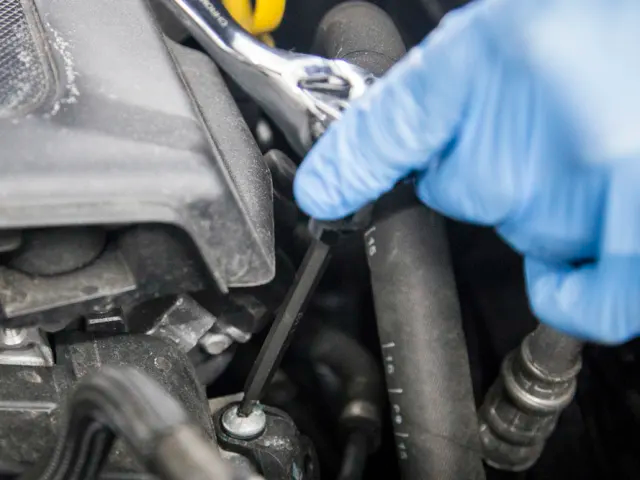 Person wearing blue gloves using a tool on car engine components.