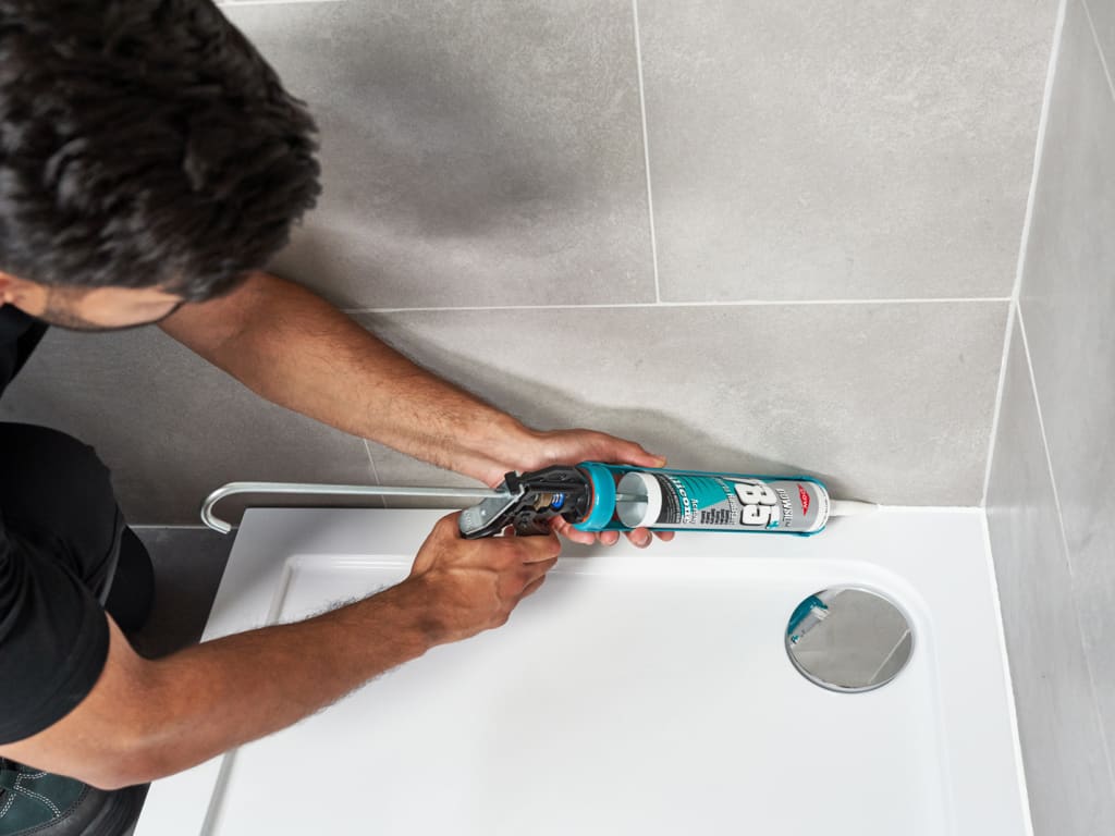 Person applying sealant to a bathroom wall with a caulking gun.