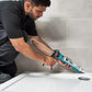 Person applying sealant to a bathroom corner with a caulking gun.