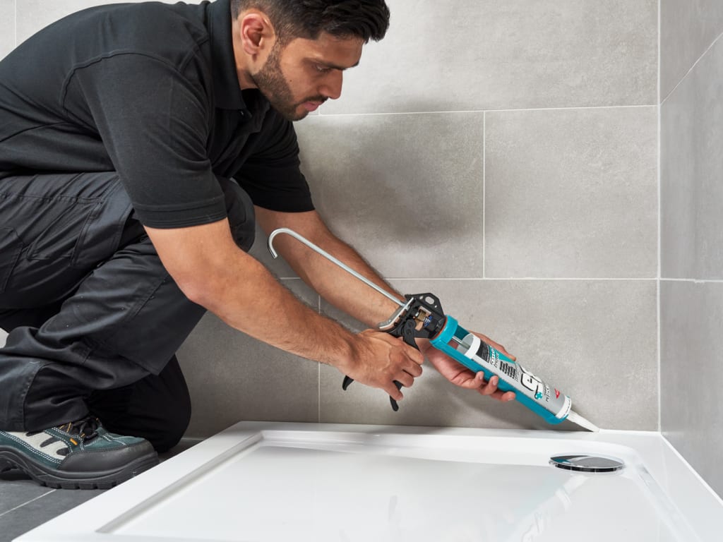 Person applying sealant to a bathroom corner with a caulking gun.
