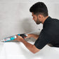 Person using a cleaning tool on a white bathtub against a tiled wall.