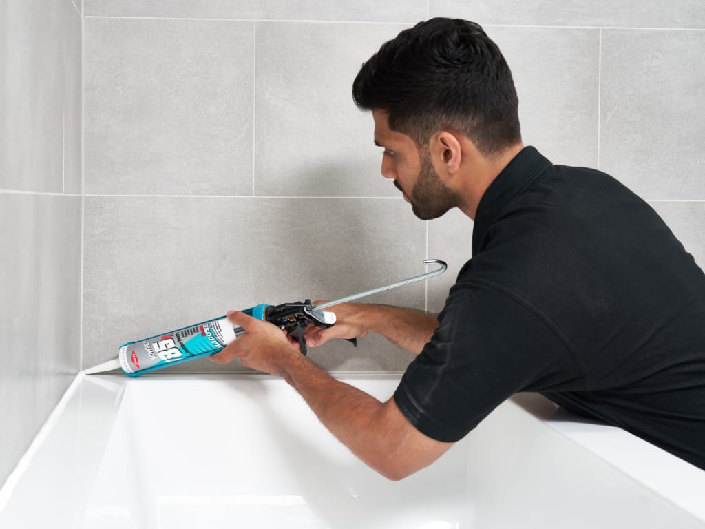Person using a cleaning tool on a white bathtub against a tiled wall.