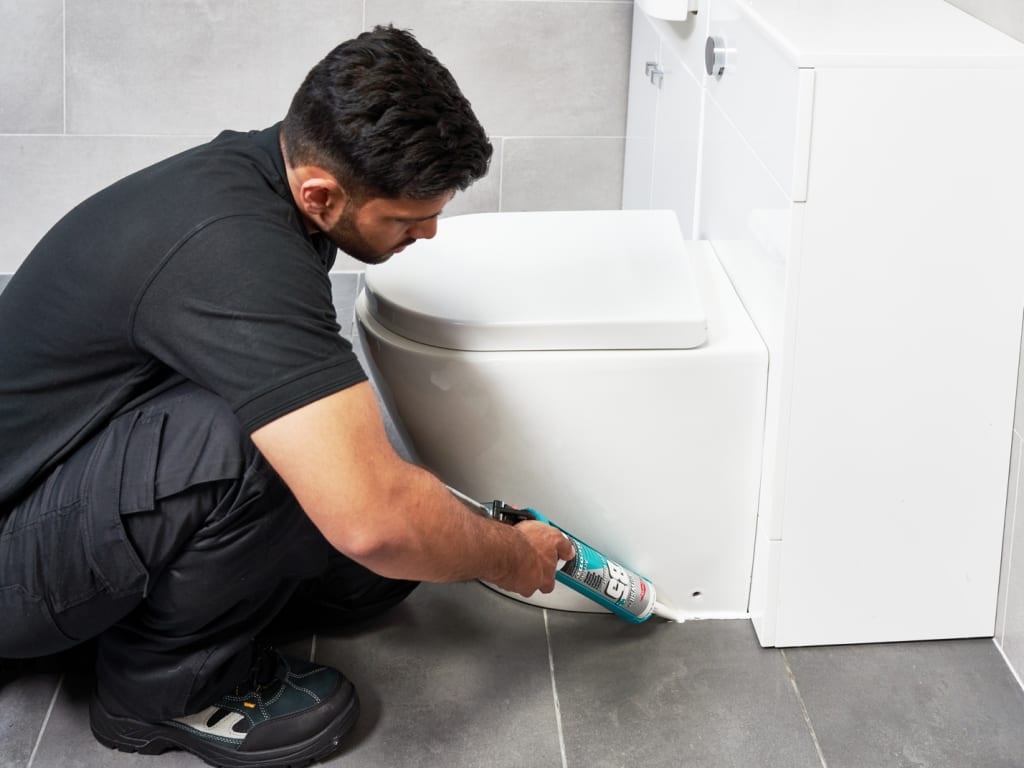 Person applying caulk to a bathroom cabinet.