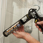 Person using a plumbers gold caulking gun in a bathroom setting