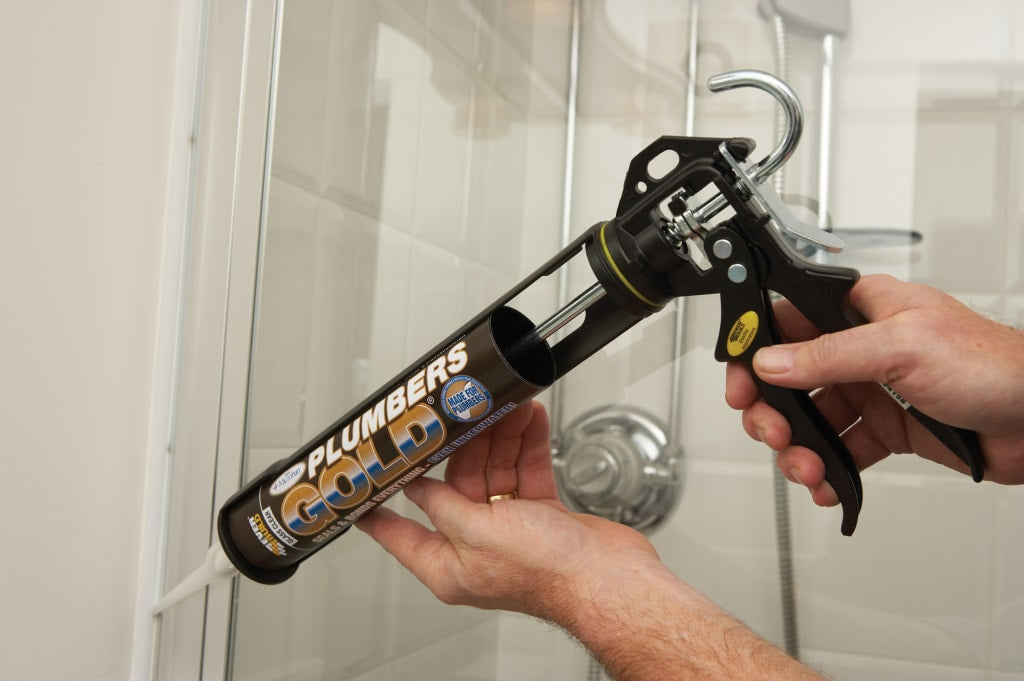 Person using a plumbers gold caulking gun in a bathroom setting
