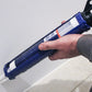 Hand holding a blue caulking gun near a white surface