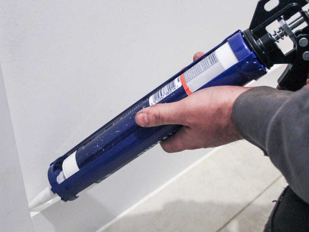 Hand holding a blue caulking gun near a white surface