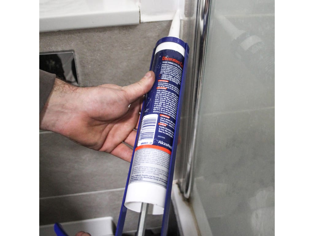 Person applying caulk to a bathroom corner with a tube of caulk.