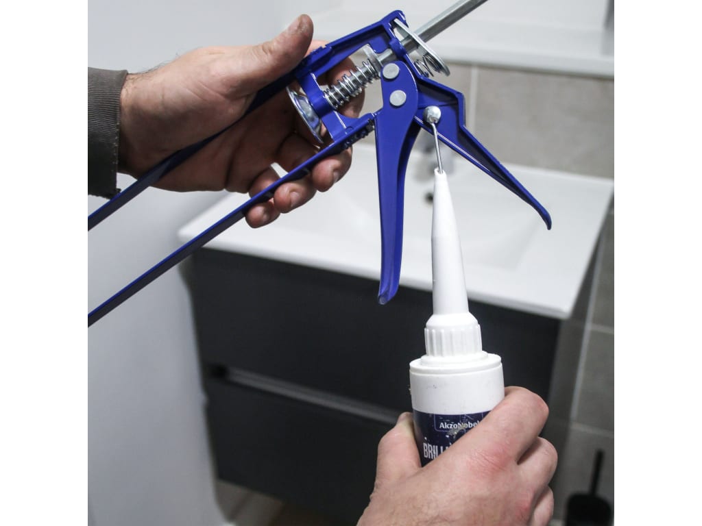 Person using a caulking gun to apply silicone sealant to a bathroom fixture.