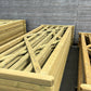 Light natural wood garden fencing panels and frames stacked outdoors against a gray wooden shed.