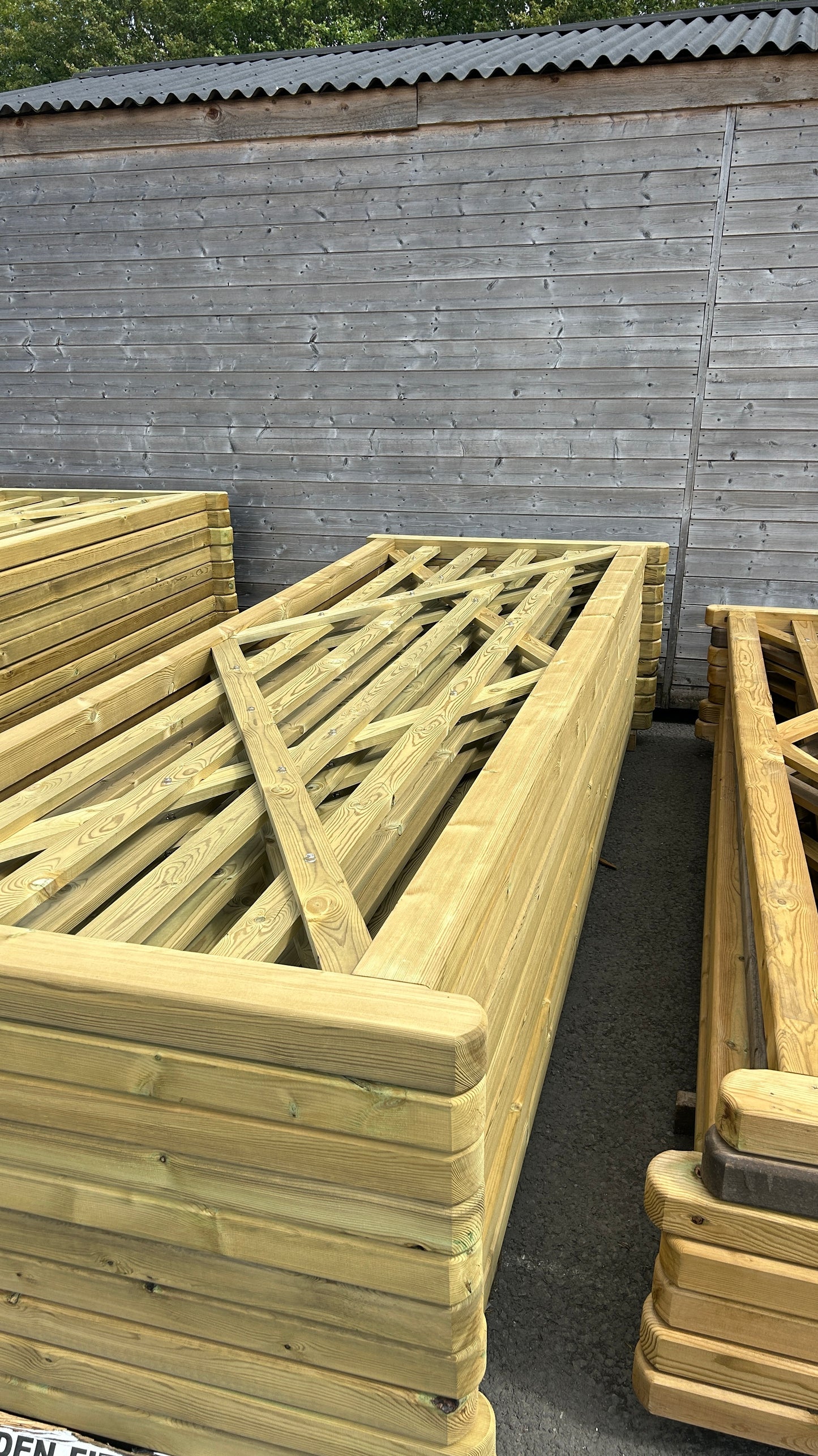 Light natural wood garden fencing panels and frames stacked outdoors against a gray wooden shed.