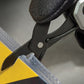 Close-up of a black plastic and silver metal tool with a textured black grip, shown pressing down on a clear strip over a yellow surface.