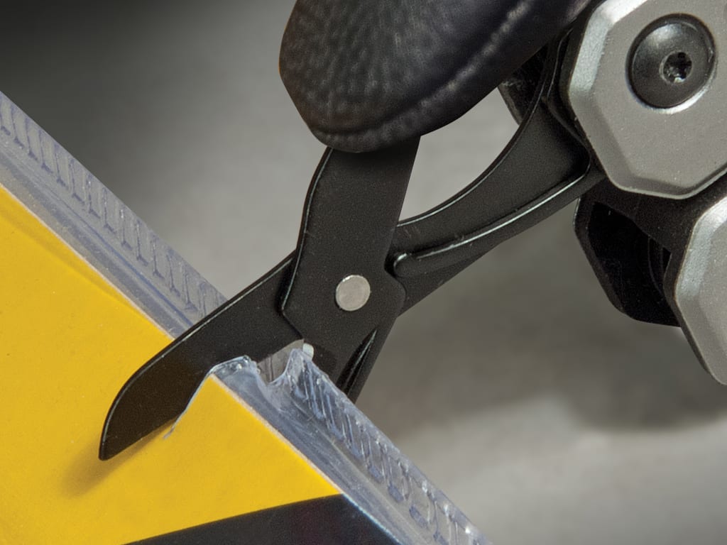 Close-up of a black plastic and silver metal tool with a textured black grip, shown pressing down on a clear strip over a yellow surface.