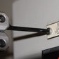 Close-up of a metal tool holding a black rod against a white machine panel with a sign reading 'BLADE LACQUER POLICEMAN' and a red digital display.