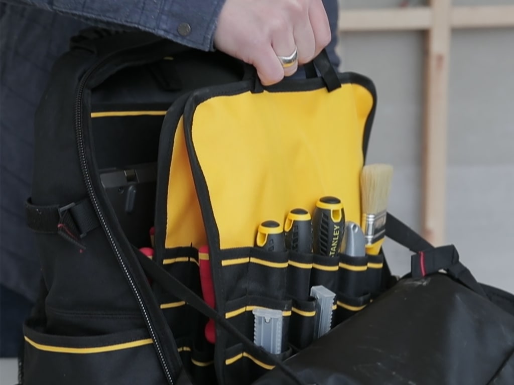 Person holding a yellow and black tool bag with tools inside.