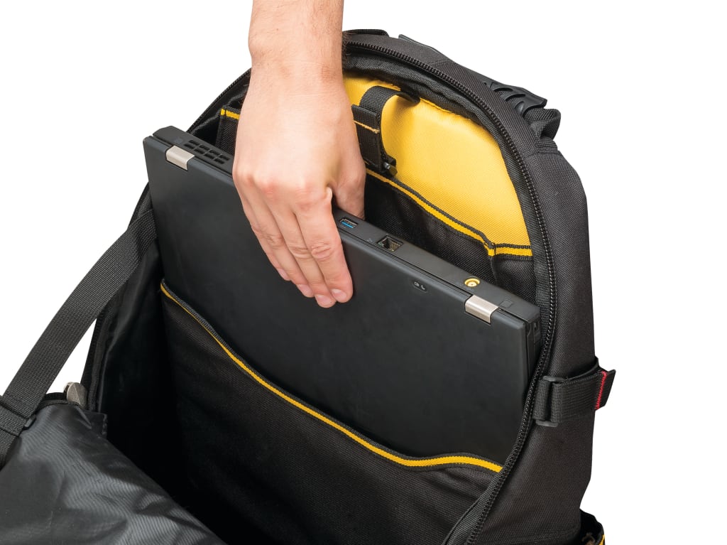 A close-up of a black laptop backpack with a person's hand inserting a closed silver laptop into the main compartment. The backpack features a bright yellow interior lining and yellow piping accents on the exterior.