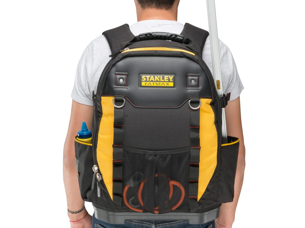 A person viewed from behind wearing a black and yellow Stanley FatMax backpack, with a white t-shirt and jeans, against a plain white background.