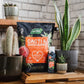 Potted plants and gardening products on a wooden surface with a brick wall background