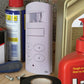 White electronic device with buttons on a wooden surface surrounded by various items including spray cans and tools.