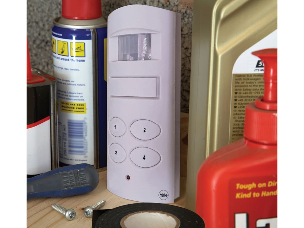 White electronic device with buttons on a wooden surface surrounded by various items including spray cans and tools.
