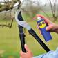 Person using WD-40 on garden shears with a blurred outdoor background