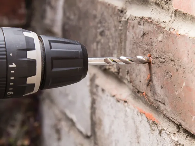 Drill bit being used to drill into a brick wall