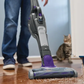 Person using a vacuum cleaner on a wooden floor with a cat watching.