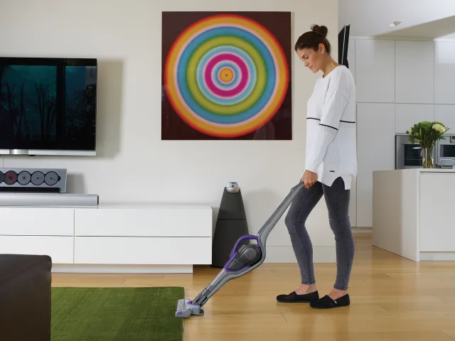 Woman using a stick vacuum cleaner in a modern living room.