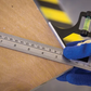 Hand wearing a blue glove using a metal ruler on a wooden surface with a blurred background.