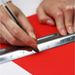 Person using a ruler and pen on a red surface