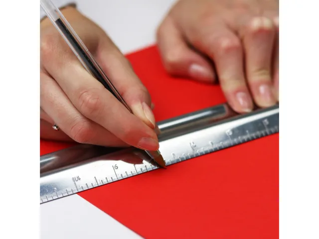 Person using a ruler and pen on a red surface