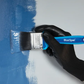 Hand wearing a black glove holding a BlueSpot brand paintbrush applying blue paint to a surface.