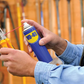 Person holding a can of WD-40 near a pair of pliers with a blurred background