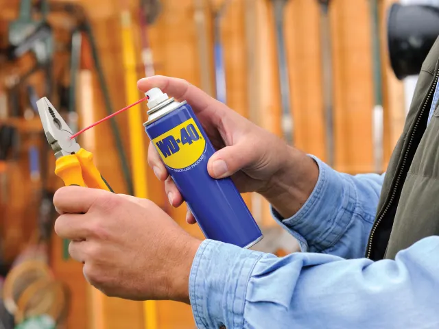 Person holding a can of WD-40 near a pair of pliers with a blurred background