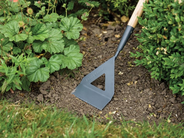 Gardening tool being used on garden soil with plants in the background