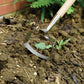 Garden cultivator in use on soil with greenery in the background