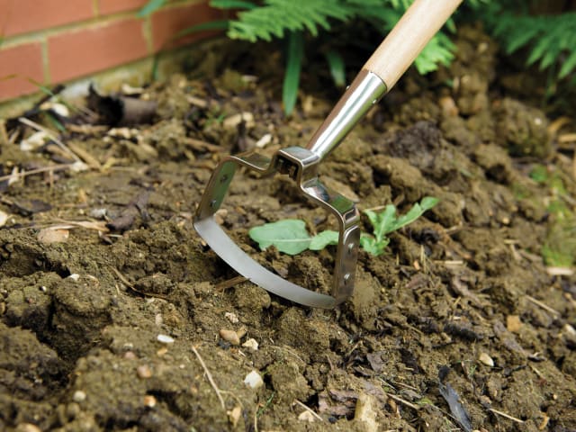 Garden cultivator in use on soil with greenery in the background