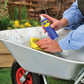 Person cleaning a wheelbarrow with a spray bottle and yellow cloth outdoors.