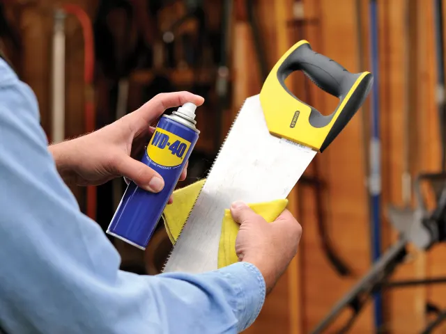 Person holding a saw and WD-40 spray can in a workshop setting