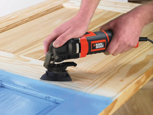 Person using a Black & Decker oscillating tool on a wooden surface