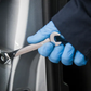 Person wearing blue gloves holding a wrench near a car door