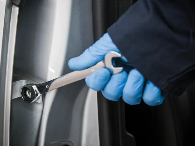 Person wearing blue gloves holding a wrench near a car door