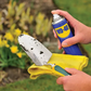 Person cleaning a garden trowel with a yellow rag and WD-40 spray in a garden setting.